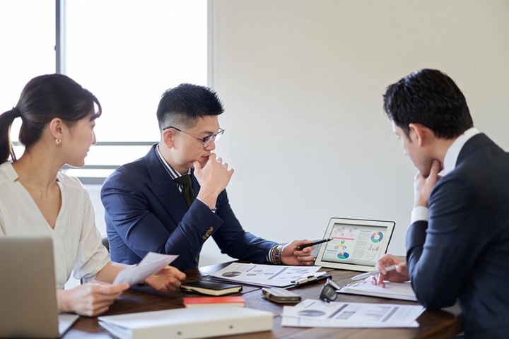 会議室でタブレットの資料を見ながら打ち合わせる3人のビジネスパーソン